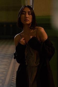 一位优雅的女人身着时尚的露肩丝绸连衣裙，在室内摆着姿势，语气喜怒无常
