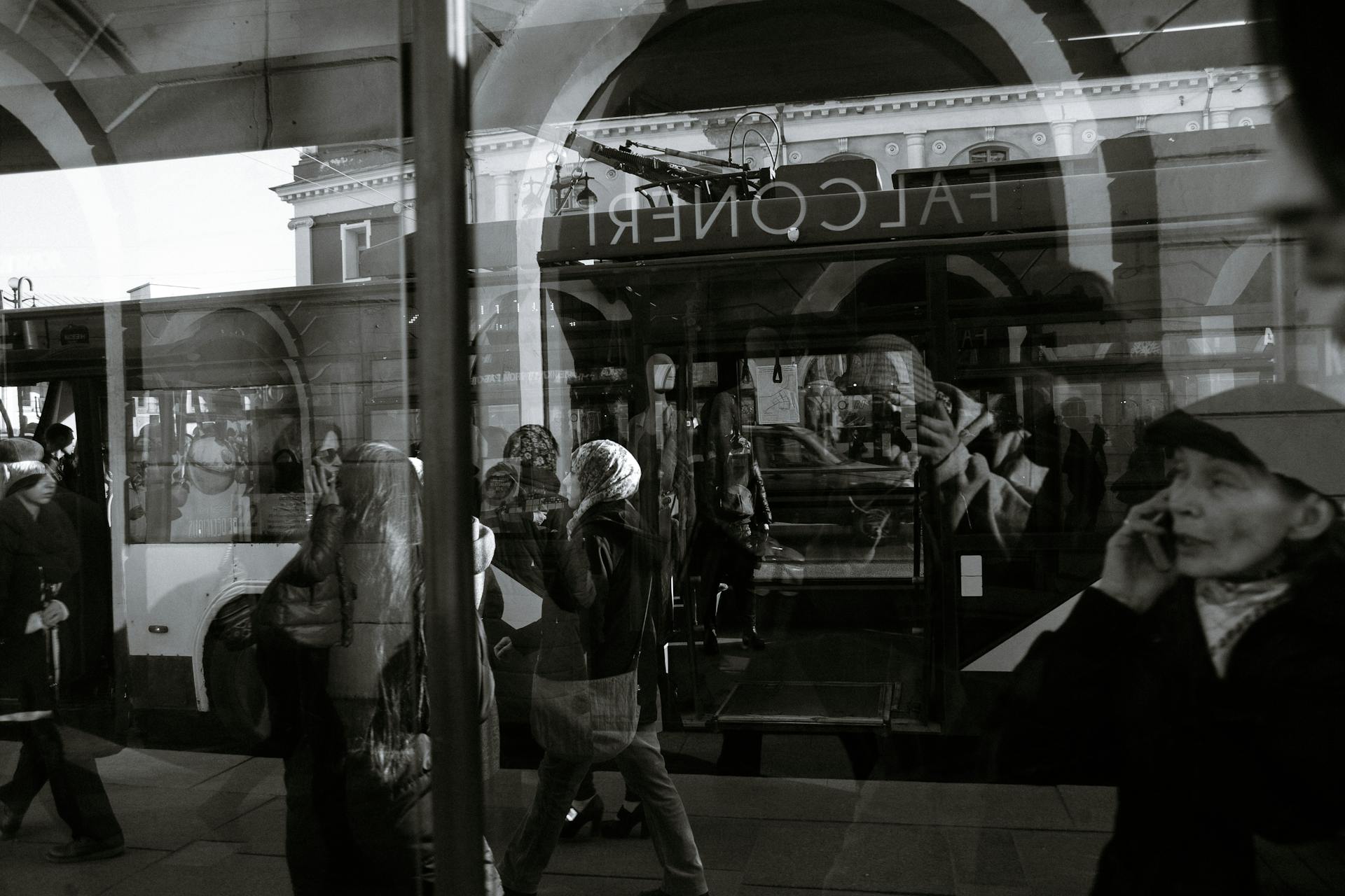 Black and white through glass wall view of anonymous passengers in trolleybus near sidewalk in town