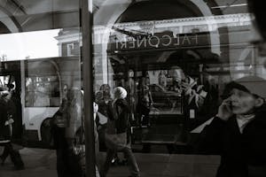Black and white through glass wall view of anonymous passengers in trolleybus near sidewalk in town