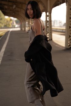一位身着优雅晚礼服的时尚女子，在复古火车站的天篷下摆着姿势