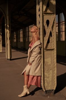 A fashionable woman in a chic outfit poses elegantly outdoors in warm sunlight.