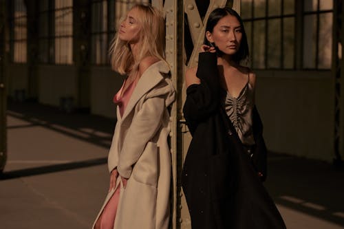 Models in Coats and Silk Dresses Under the Steel Column of a Warehouse