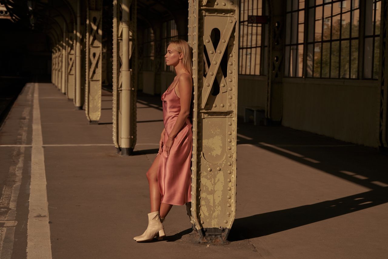 stylish woman in silk dress poses at a train station in natural light