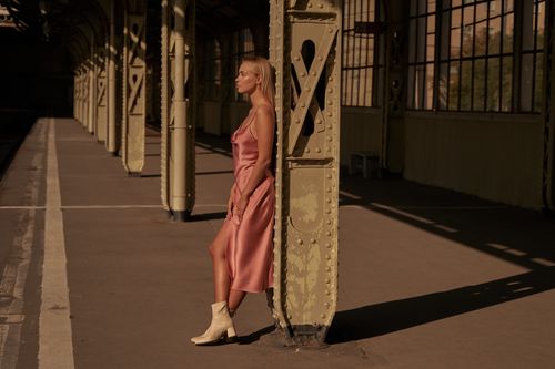 Free Stylish woman in silk dress poses at a train station in natural light. Stock Photo