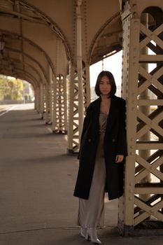 一位时尚女子穿着黑色外套在老式铁路结构下摆姿势