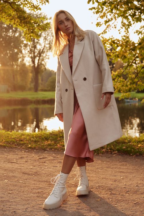 Free Elegant woman in trench coat poses by a serene pond during autumn sunset. Stock Photo