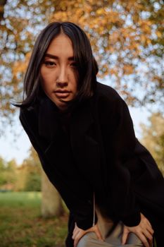 一位身穿黑色外套的年轻亚洲女子在秋日户外摆姿势