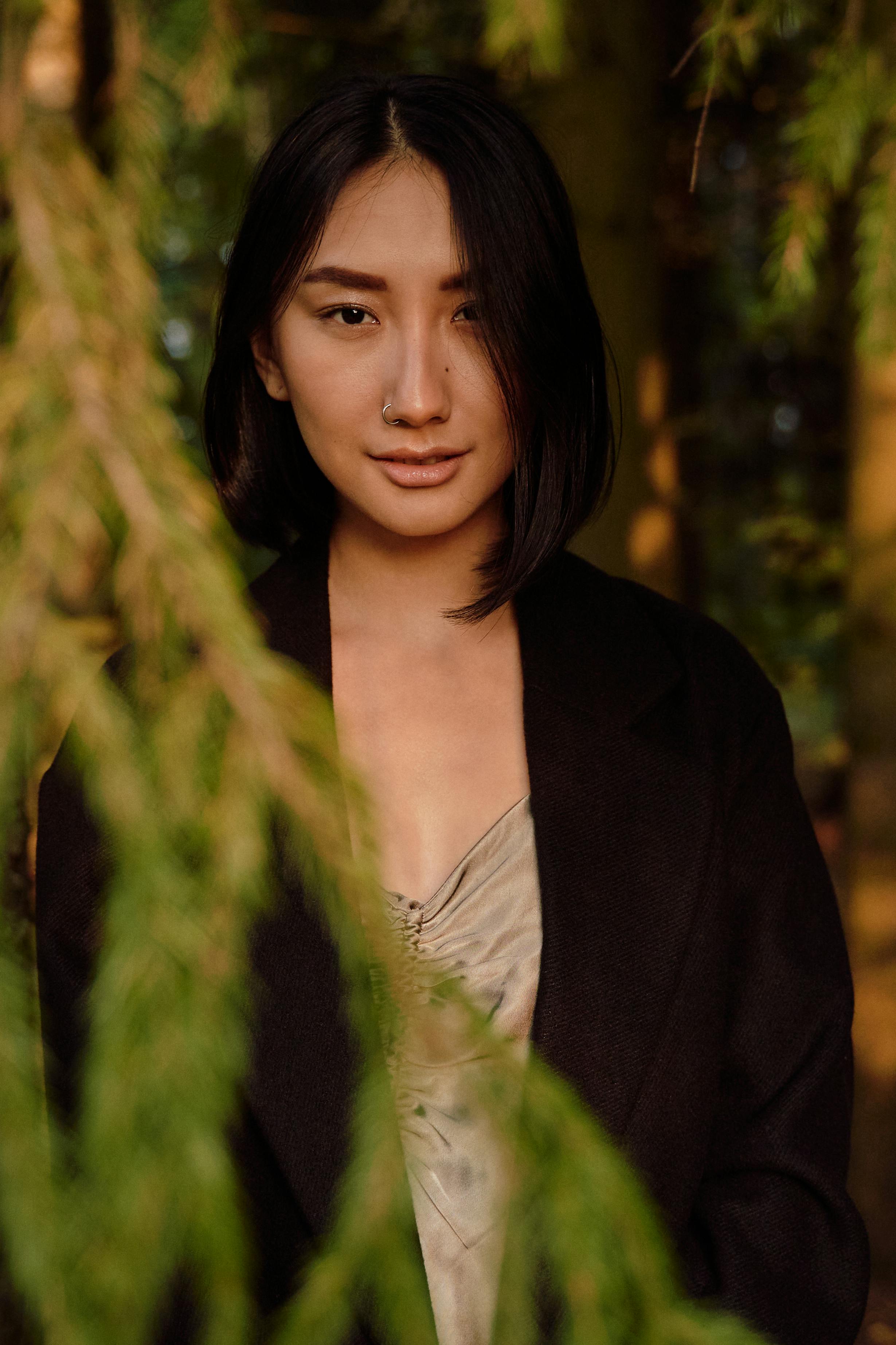 一位年轻女子的特写肖像，她戴着鼻环，周围环绕着绿色植物
