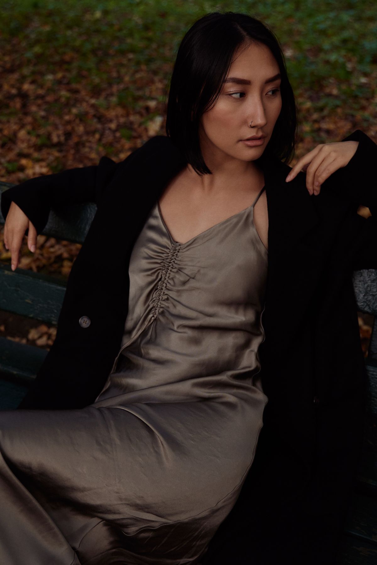 A woman in a gray dress with a black coat, looking over her shoulder
