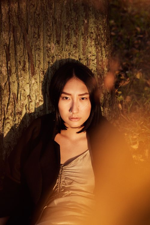 Free Portrait of a young woman with a nose piercing leaning against a tree trunk in the warm sunset light. Stock Photo