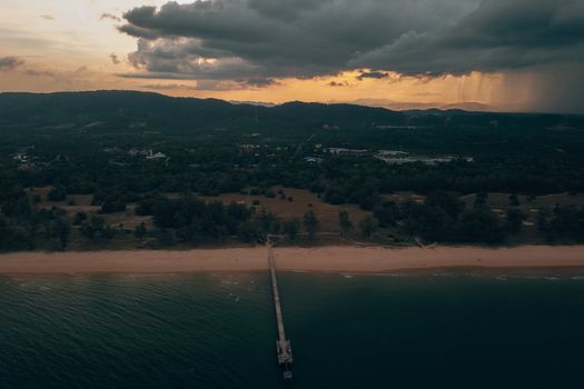 Aerial view of long platform in water of sea leading to sandy coast with green woods