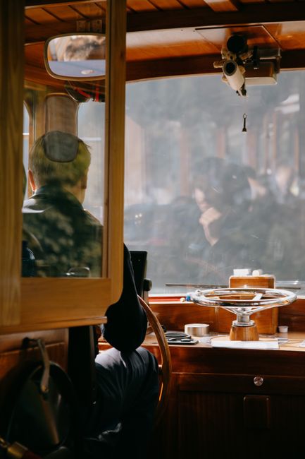 Back view of man sitting in wooden cabin with shiny ship wheel while sailing yacht in sunlight