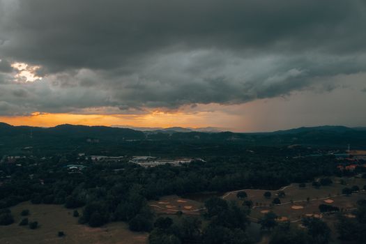 Aerial view of settlement surrounded by green woodland under clouds in overcast weather