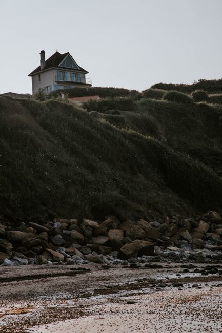 Low angle of remote small house on green grassy hill above peaceful shore of sea