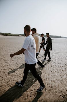 Four men enjoying a leisurely walk on a sunny beach, embracing friendship and relaxation.
