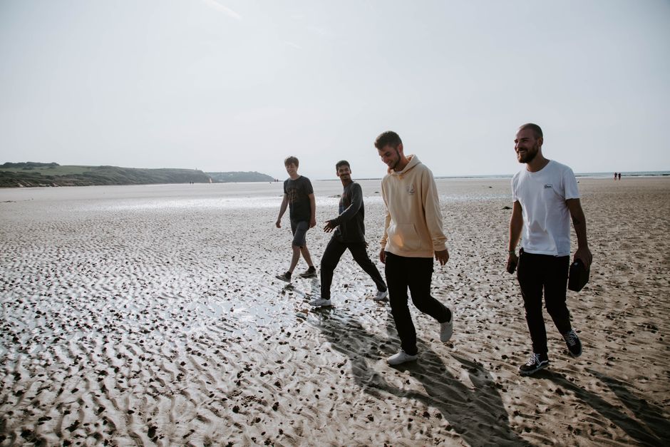 Four friends enjoy a relaxing walk on a sunny beach, embodying leisure and happiness.