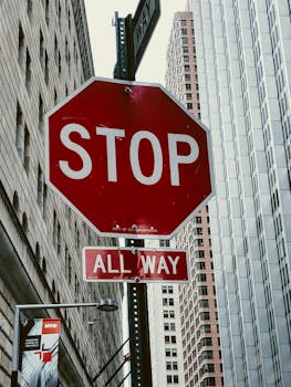 Close-up of a stop sign at an intersection in New York City with skyscrapers in the background.