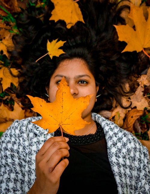 Free A woman lies beneath autumn leaves, holding a maple leaf over her face, embodying fall's essence. Stock Photo