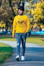 A Man on Yellow Sweater and Ripped Jeans Walking on Concrete Pathway
