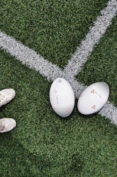 Two rugby balls placed on a grass field with visible lines, shot from above.