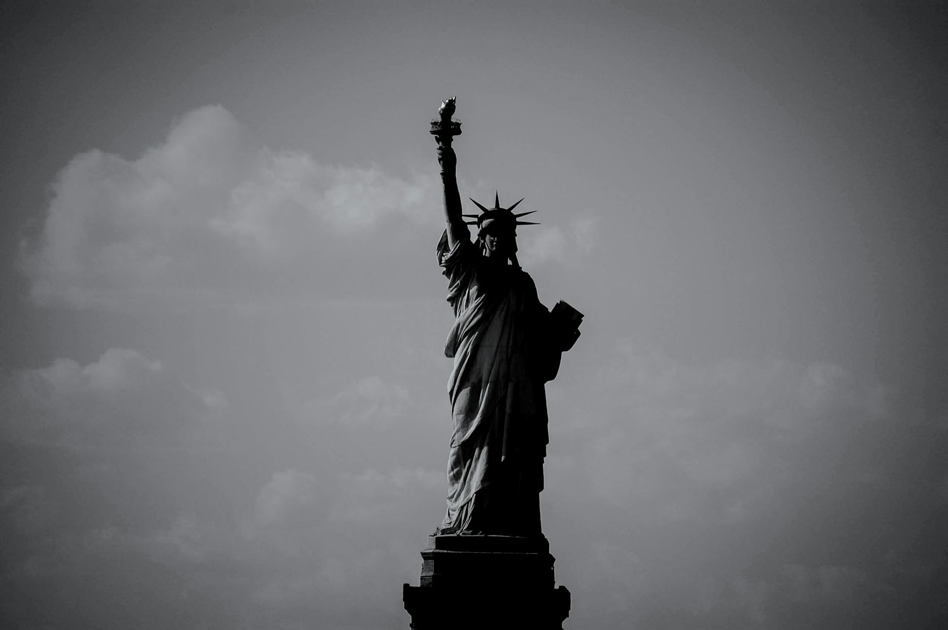 Dramatic black and white silhouette of the Statue of Liberty with a cloudy sky.