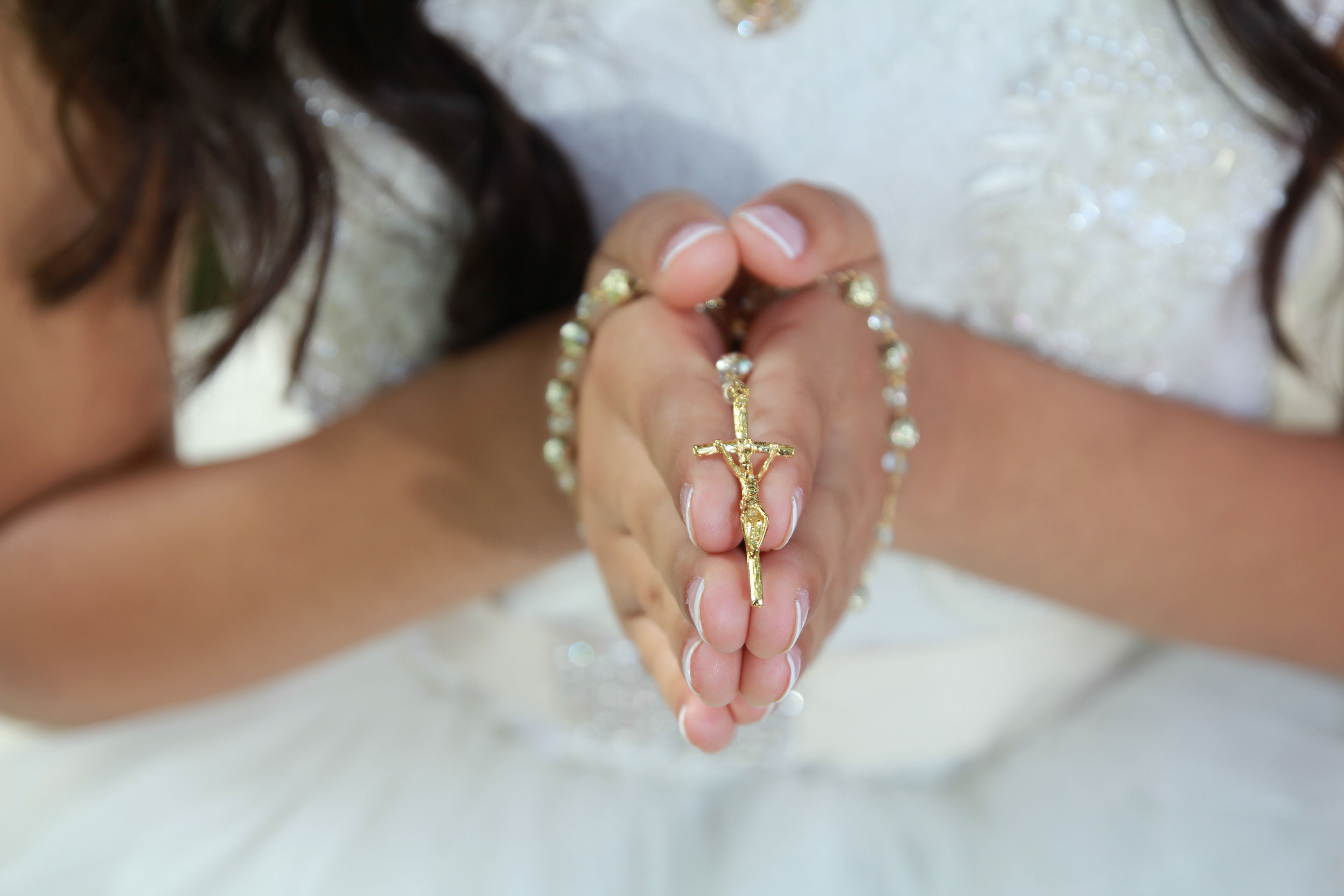 Hands holding a small cross and rosary together