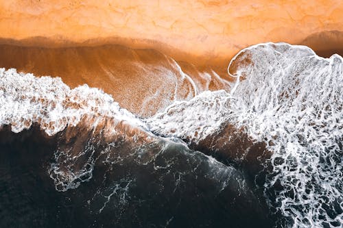 Drone view of foamy waves of fast ocean water rolling on sandy beach