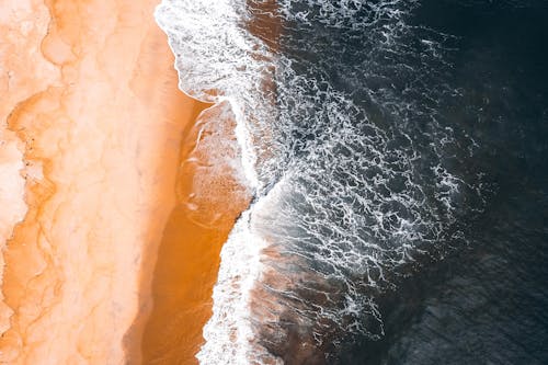 Aerial view of wavy ocean rolling on sandy beach in tropical country in daylight
