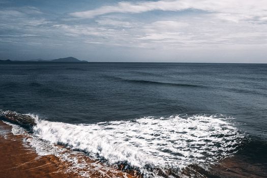 多云的天空下，是一片和平的海景，有温柔的海浪和沙质海岸线