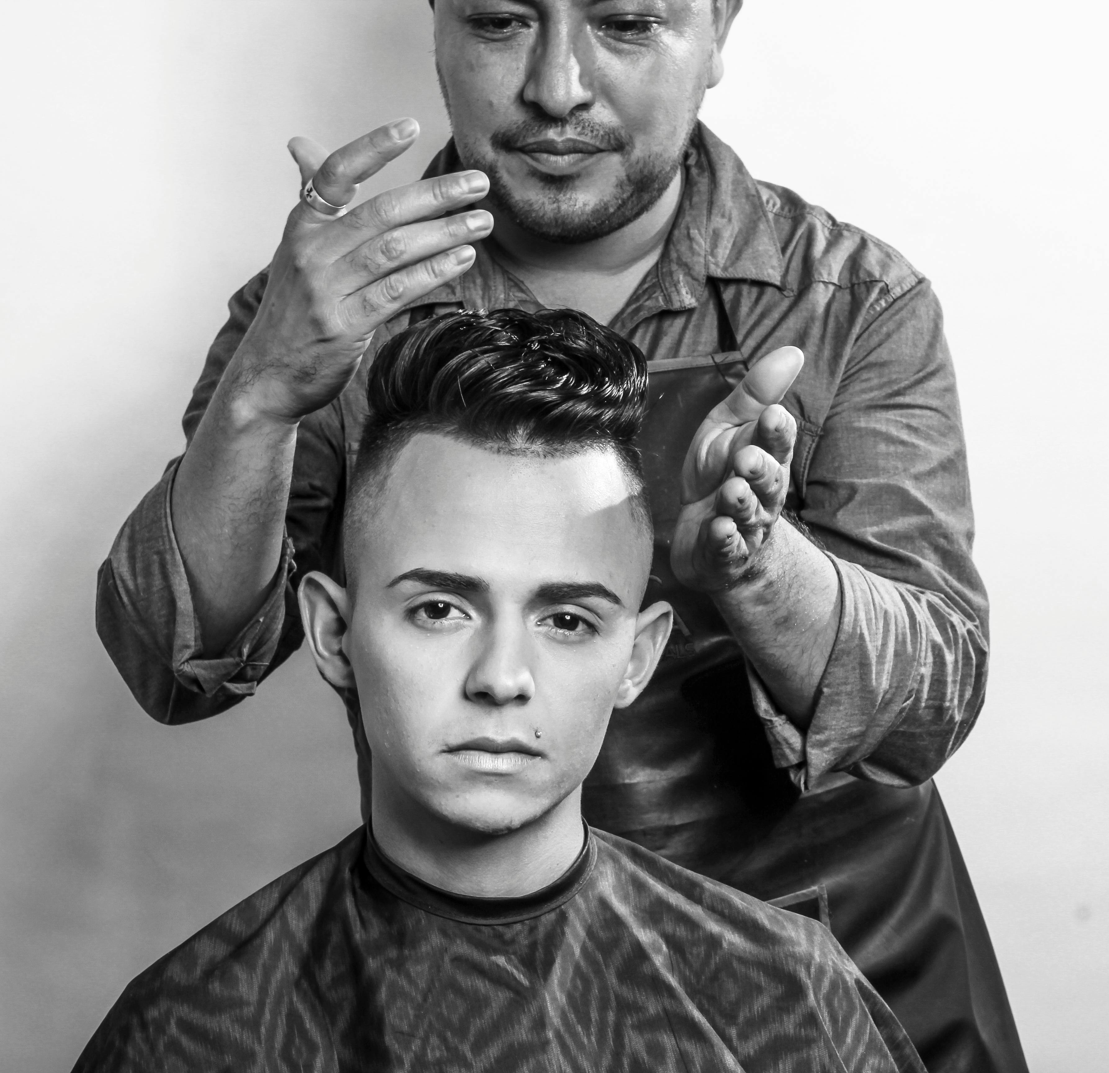 A hairstylist carefully styles a young man's hair in a professional salon setting, emphasizing modern grooming techniques.