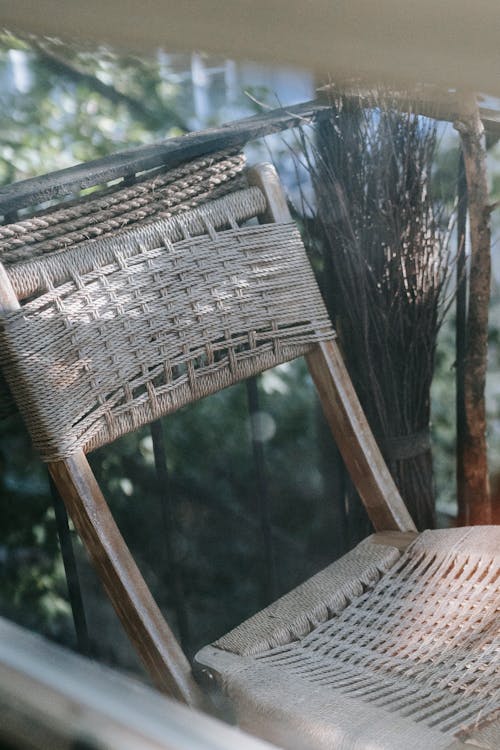 Free Through glass view of old cane chair with ornament on fenced terrace near tree in daytime Stock Photo
