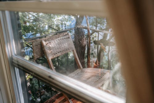 Free Through glass view of aged cane chair on fenced balcony in countryside house in daylight Stock Photo
