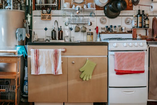 Sink with cabinet under shelves with frying pans and bottles in kitchen with ceramic wall