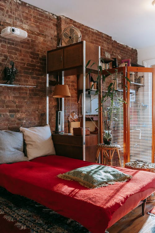 Free Interior of cozy room with comfortable bed near stylish stone wall and work zone decorated with various potted plants Stock Photo