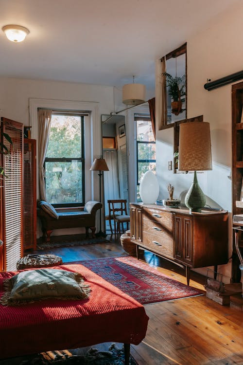 Interior of stylish vintage styled room with comfortable bed and classic wooden cabinet decorated with lamps and plants in sunlight