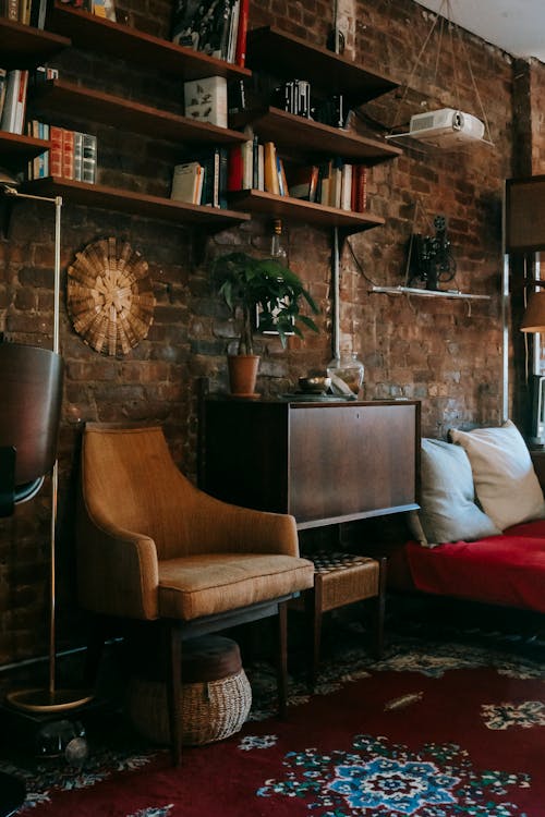 Interior details of cozy apartment with wooden cabinet and comfortable armchair placed near brick wall decorated with bookshelves and potted plant