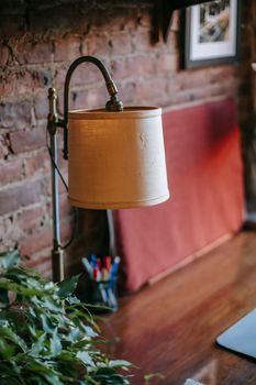 From above of elegant vintage lamp placed on wooden table with green plant near shabby brick wall