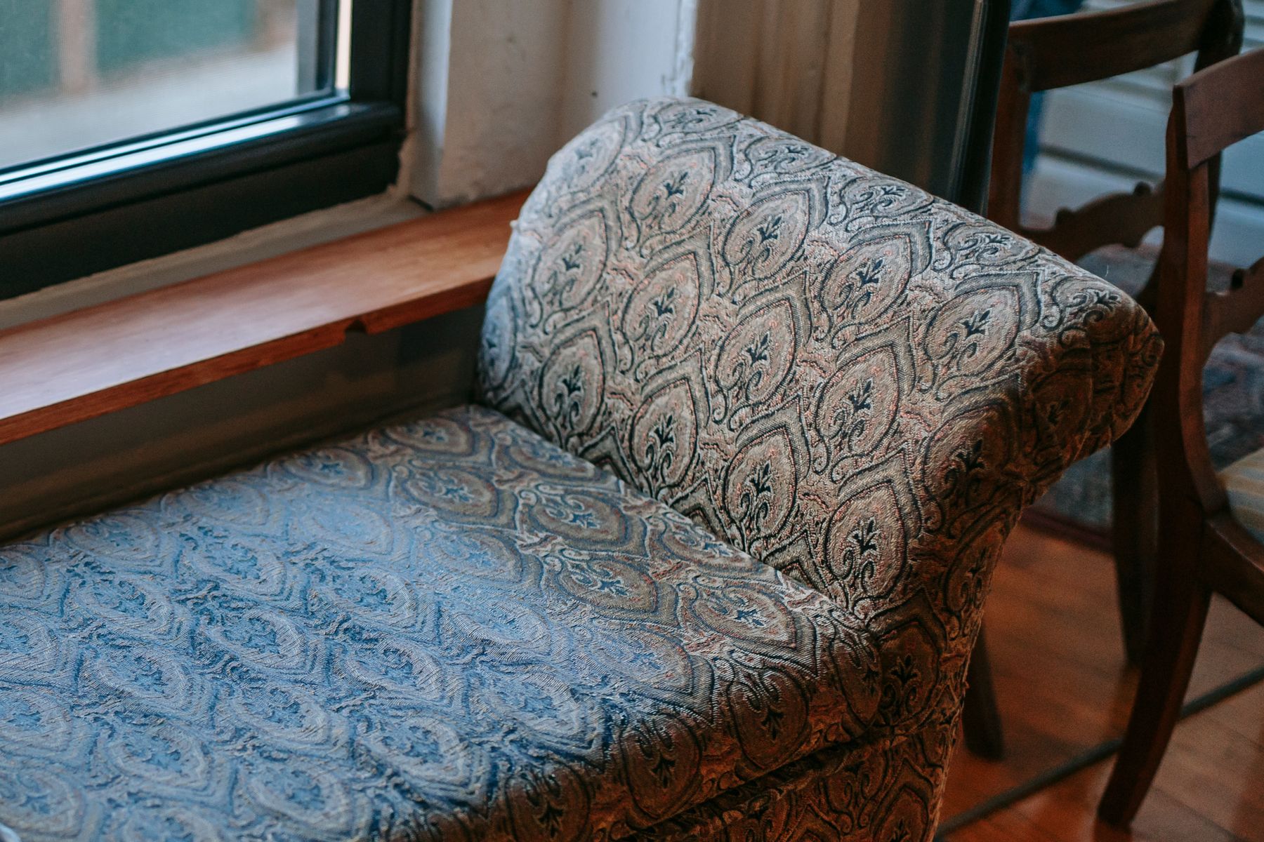 Vintage upholstered ottoman bench positioned close to a glazed window