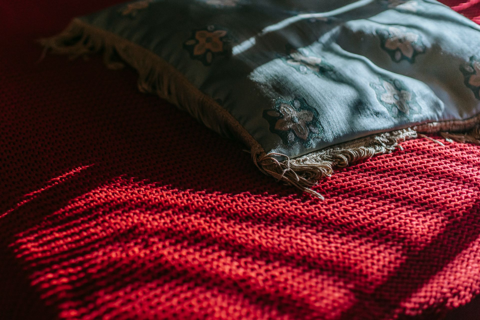 Warm sunlight on a cozy red blanket with a decorative pillow indoors.