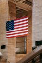 From below of Grand Central Terminal station in New York main hall interior with national USA flag hanging between brick columns