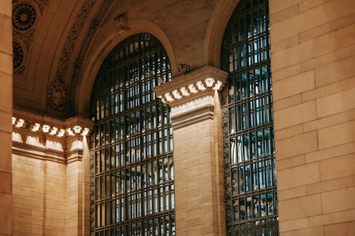 From below of illuminated interior of Grand Central Terminal station with high decorated ceiling and big windows with pillars in New York USA