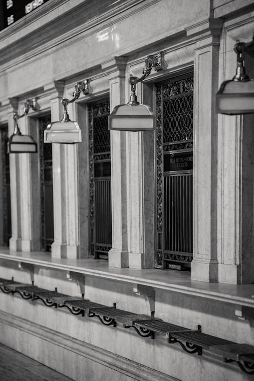 Black and white of old metal ticket windows in stone walls of railway station