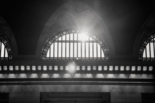 Free From below black and white of sun shining through ornamental arched windows with bas relief above located inside spacious hall of historic building Stock Photo