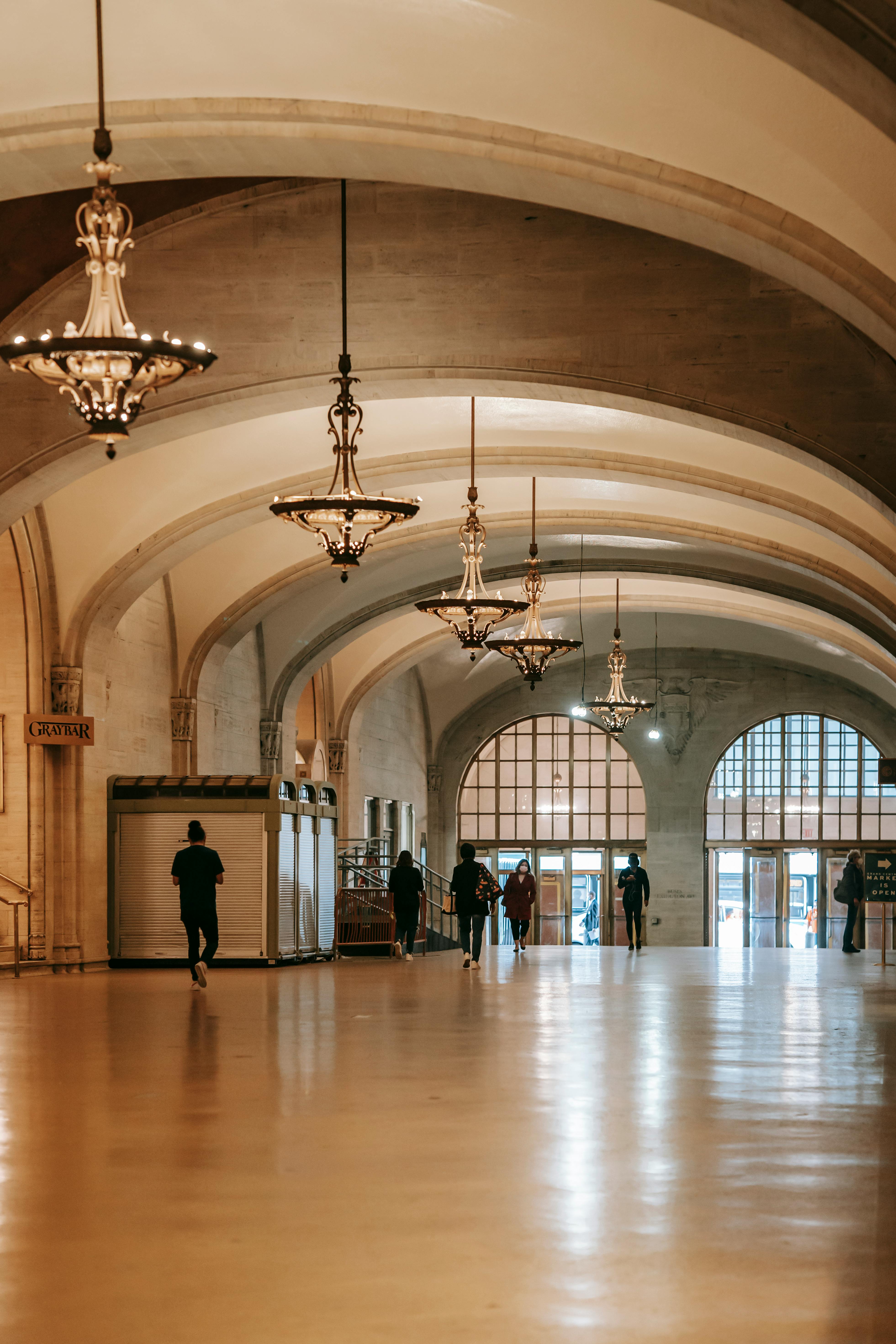 people walking along arched passage with glass chandeliers