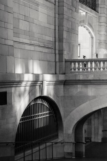 Black and white exterior of historic stone building with balcony and arch located on street