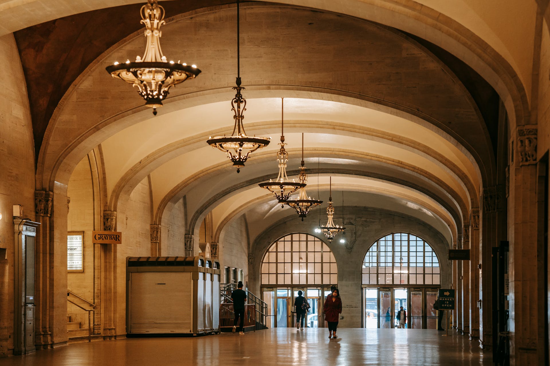 Aged house interior with shiny passage and columns under arched vaults with hanging chandeliers above unrecognizable people