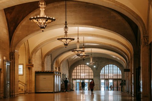 Free Aged house interior with shiny passage and columns under arched vaults with hanging chandeliers above unrecognizable people Stock Photo