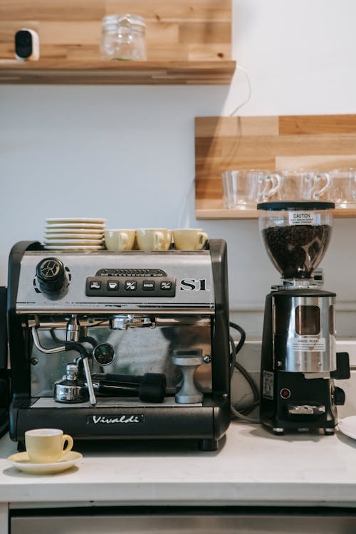 Free Modern stainless coffee machine placed on counter in kitchen under shelves with coffeemaker and ceramic mugs Stock Photo