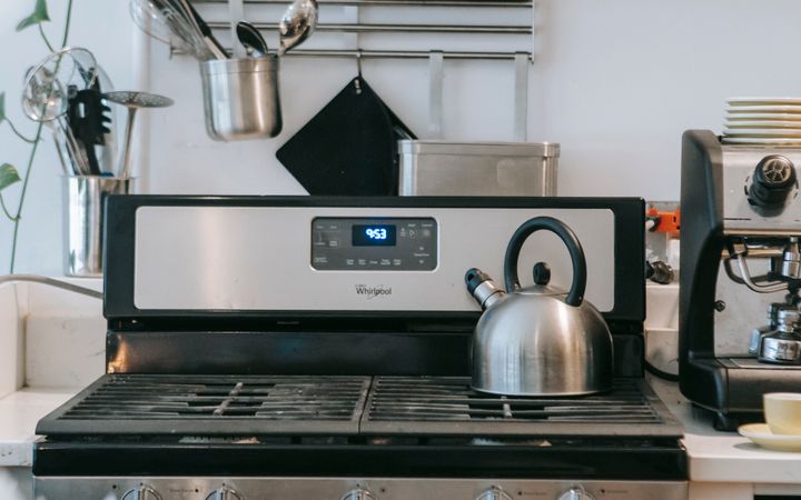 Interior of contemporary light kitchen with gas stove with kettle surrounded with various kitchenware