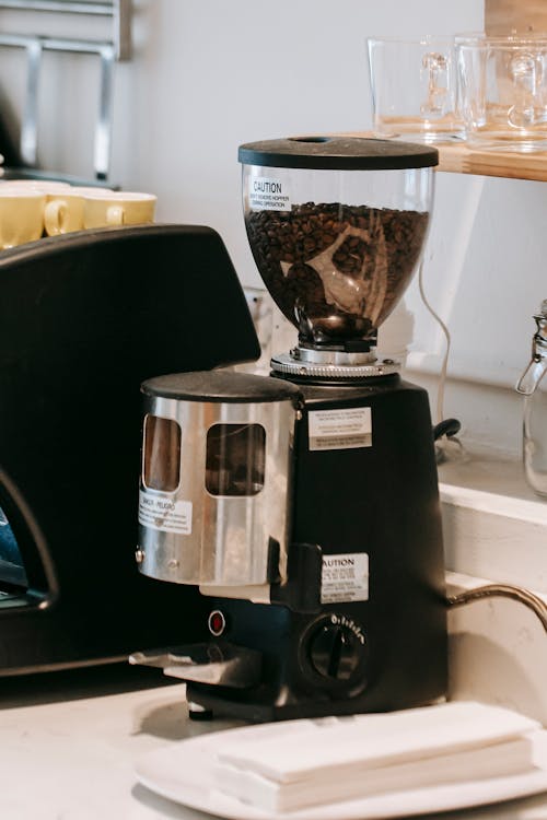 Contemporary coffee grinder placed on kitchen counter near coffee machine in modern light kitchen